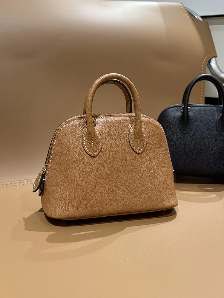 Small tan dome shaped bag with twin rounded top handles and a zip closure